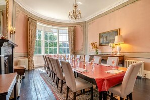 Ein formeller Speisesaal mit einem langen Tisch, gedeckt für eine Mahlzeit, umgeben von Stühlen, einer Kronleuchter und einem Kamin.