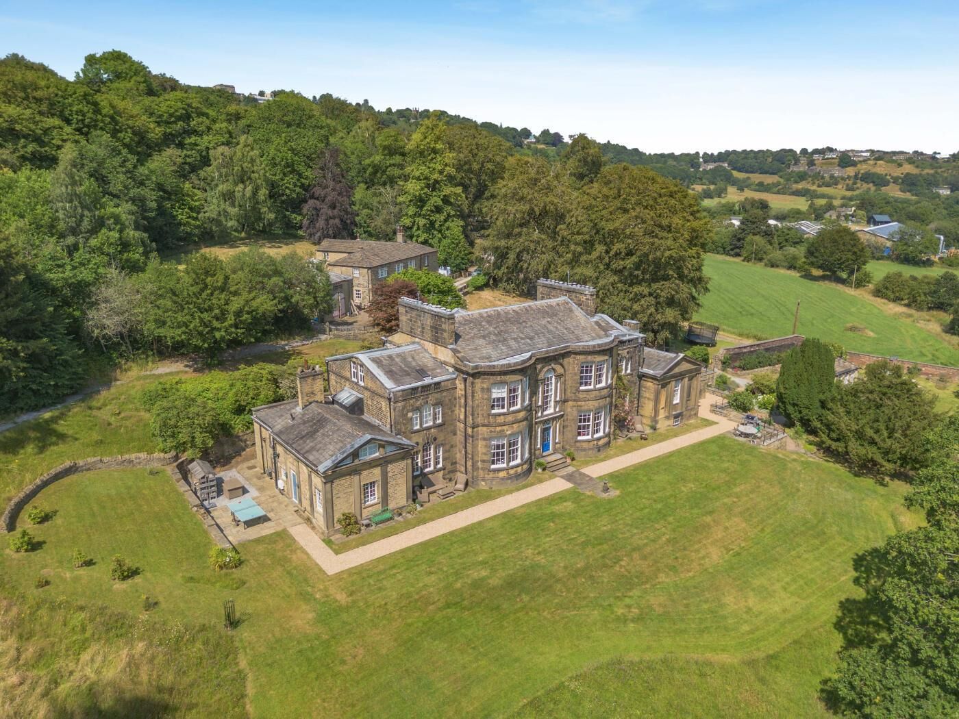 A large, historic stone building with multiple wings, surrounded by a well-maintained lawn and trees.