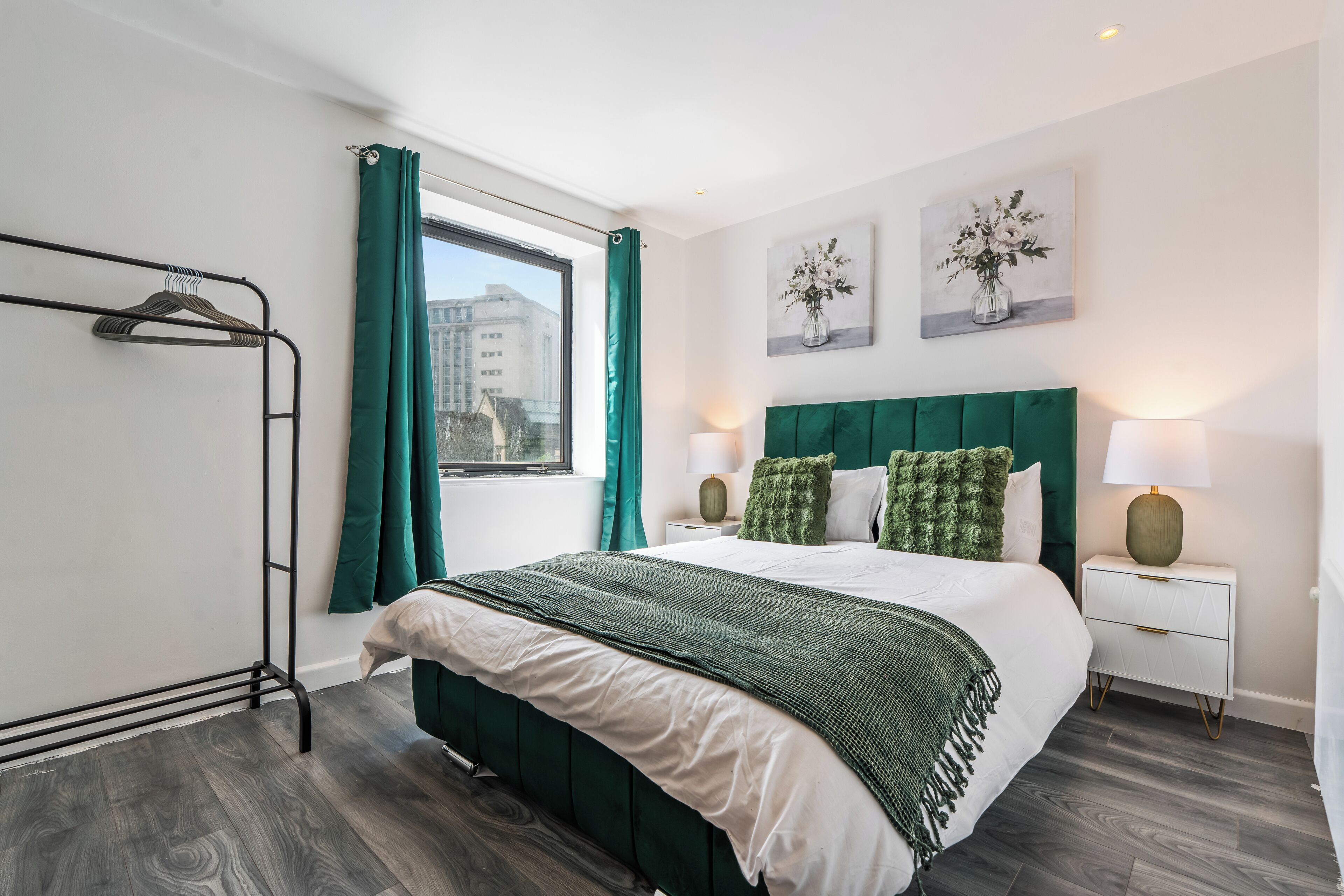 A modern bedroom with a bed, green curtains, a window, and a nightstand with a lamp.