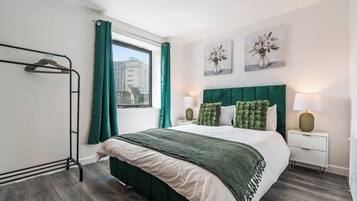 A modern bedroom with a bed, green curtains, a window, and a nightstand with a lamp.