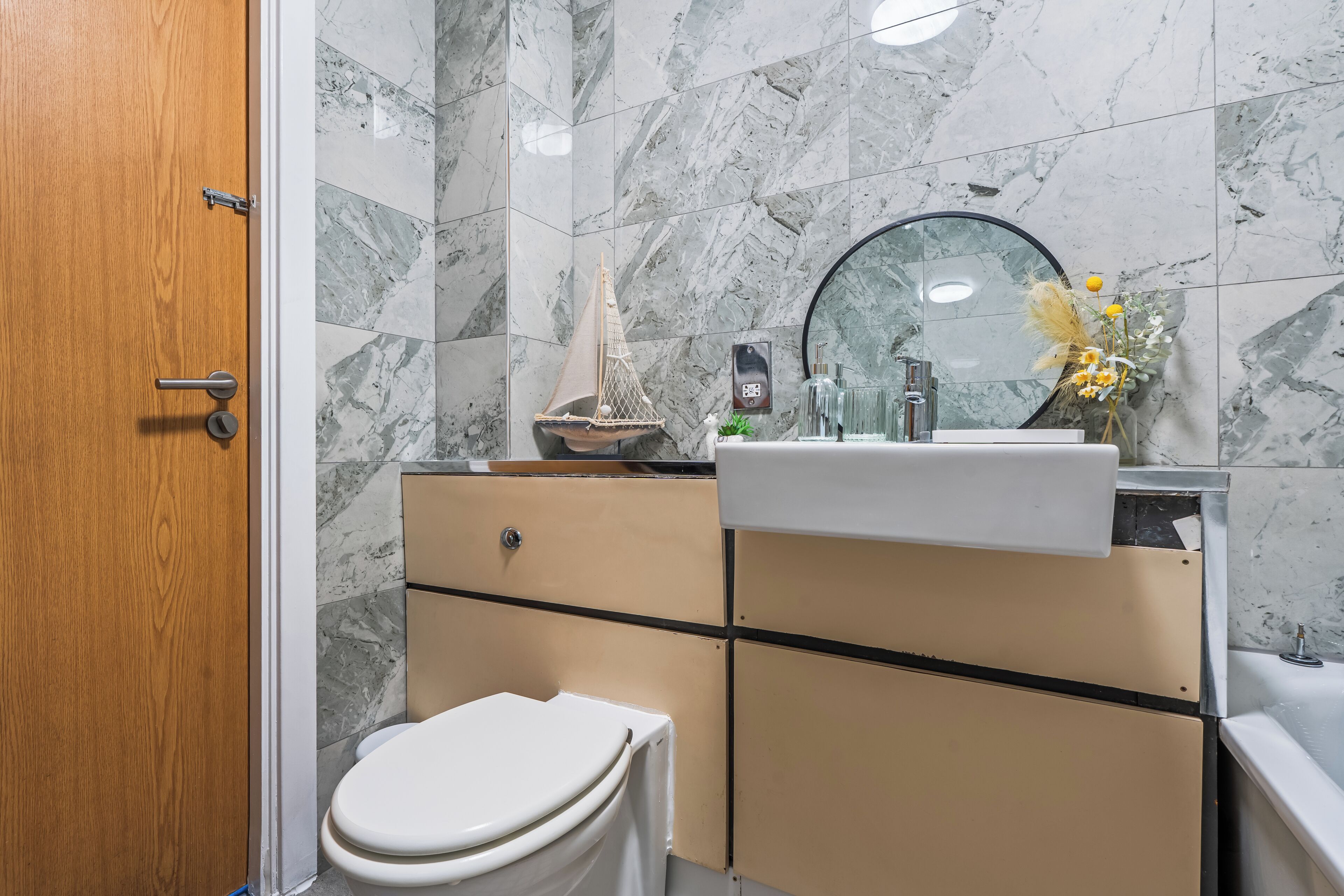 Une salle de bain avec une porte en bois, des toilettes, un lavabo avec un miroir et une maquette de bateau décorative.