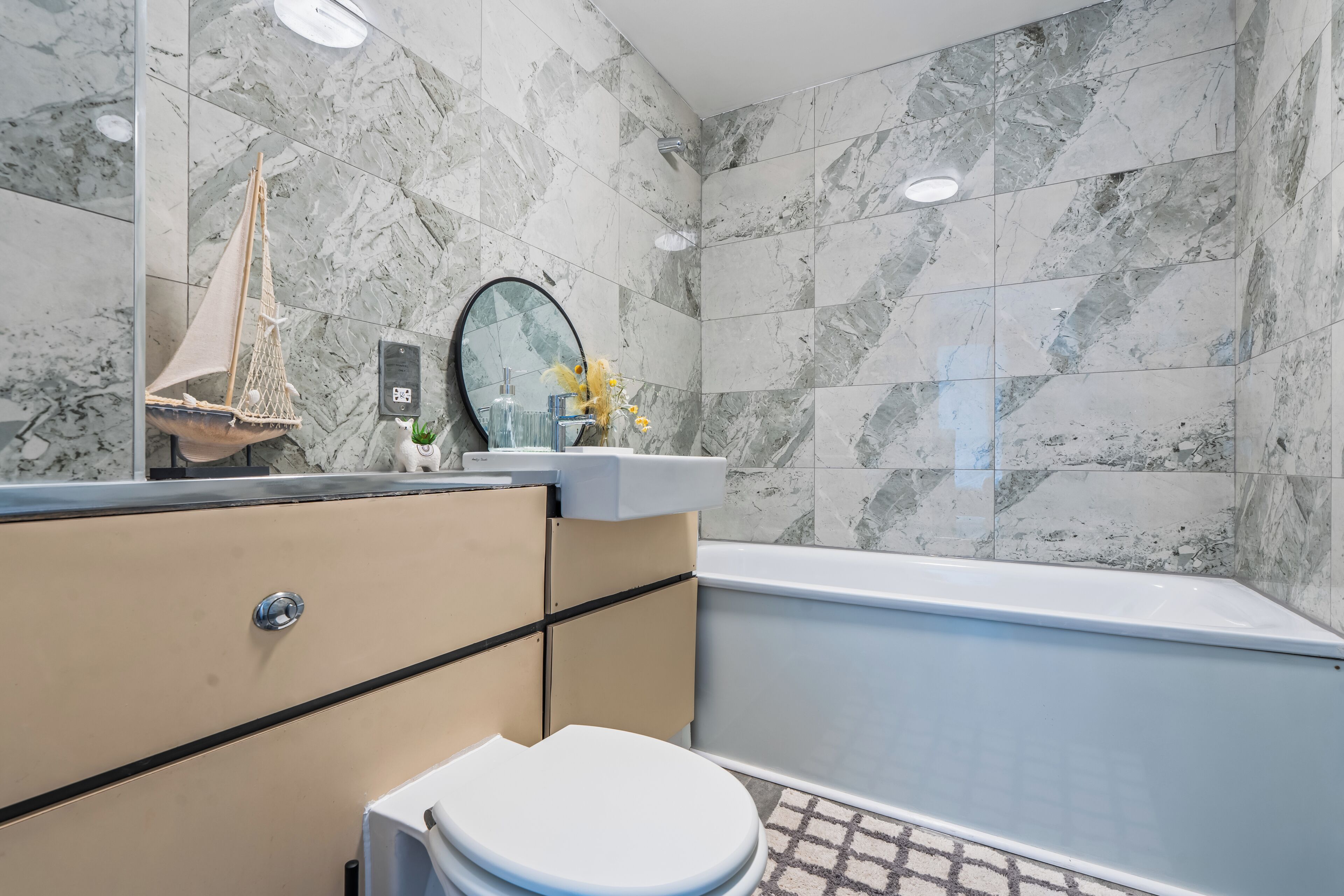 Un baño con pared de mármol, una bañera, un inodoro, un tocador con espejo y una reproducción decorativa de un barco.