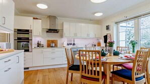Una cocina moderna con armarios blancos, una mesa de comedor de madera con sillas, y un ventanal que proporciona luz natural.
