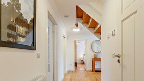 Un pasillo con suelo de madera, paredes blancas y una escalera de madera.