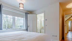 Un dormitorio con una cama grande, una ventana con cortinas, una puerta que da a un baño y suelo de madera.