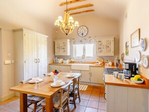 A kitchen with wooden cabinets, a dining table set for four, a chandelier, and a clock on the wall. - 2 Bed in York (oc-g0154) (Ellerton)