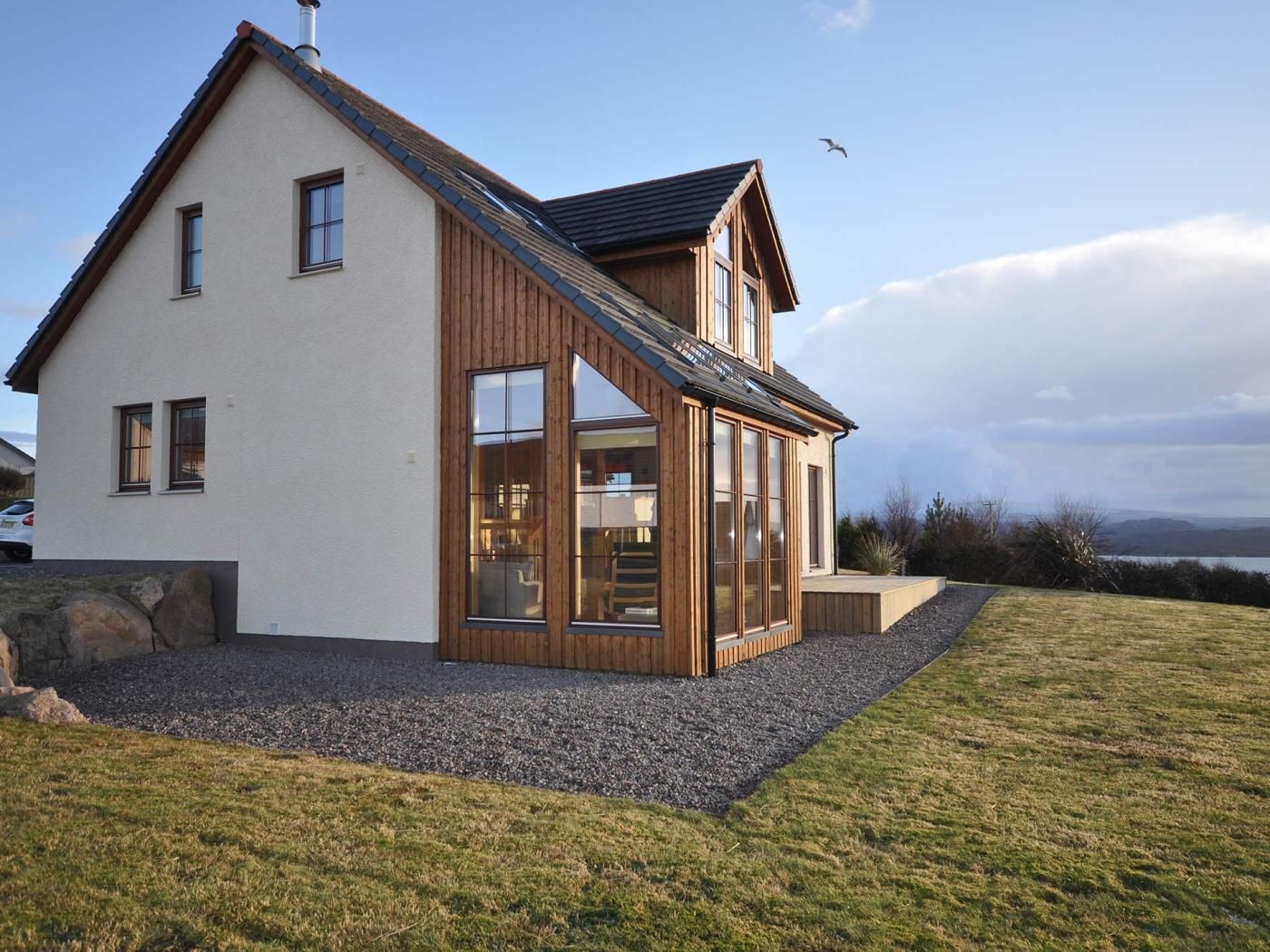 Une maison moderne à deux étages, dotée d’un toit en pente, de grandes fenêtres et offrant une vue sur le paysage.