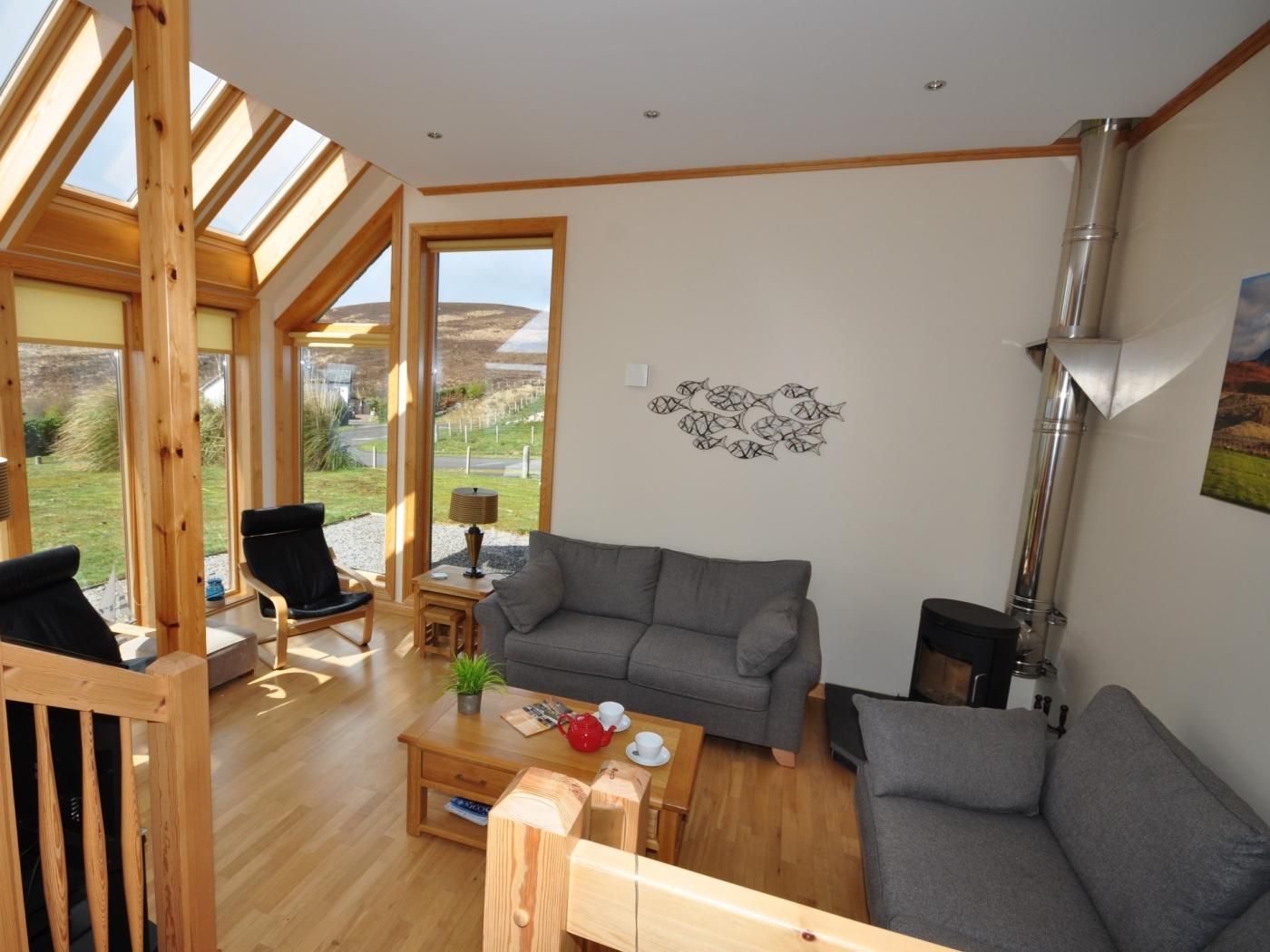 A modern living room with a grey sofa, wooden coffee table, and a view of the outdoors through large windows.
