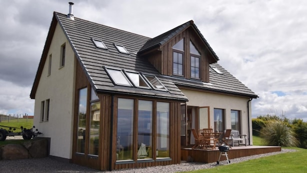Una casa moderna con amplios ventanales, techo inclinado y terraza con mobiliario exterior.