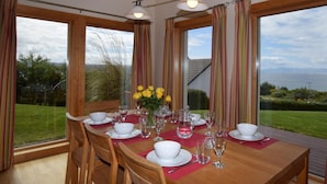 Un comedor con mesa dispuesta para cuatro, ventanas amplias y vista al mar.