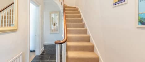 A staircase with a wooden handrail and beige carpeted steps, leading to a room with a white door and a mirror on the wall.
