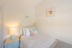 Ein Schlafzimmer mit Bett, Nachttisch mit Lampe, gerahmtem Bild an der Wand und Zierkissen.