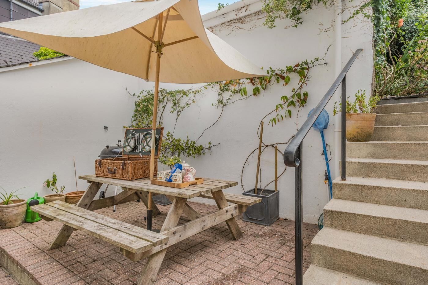 A wooden picnic table with a canopy, surrounded by potted plants and a basket.