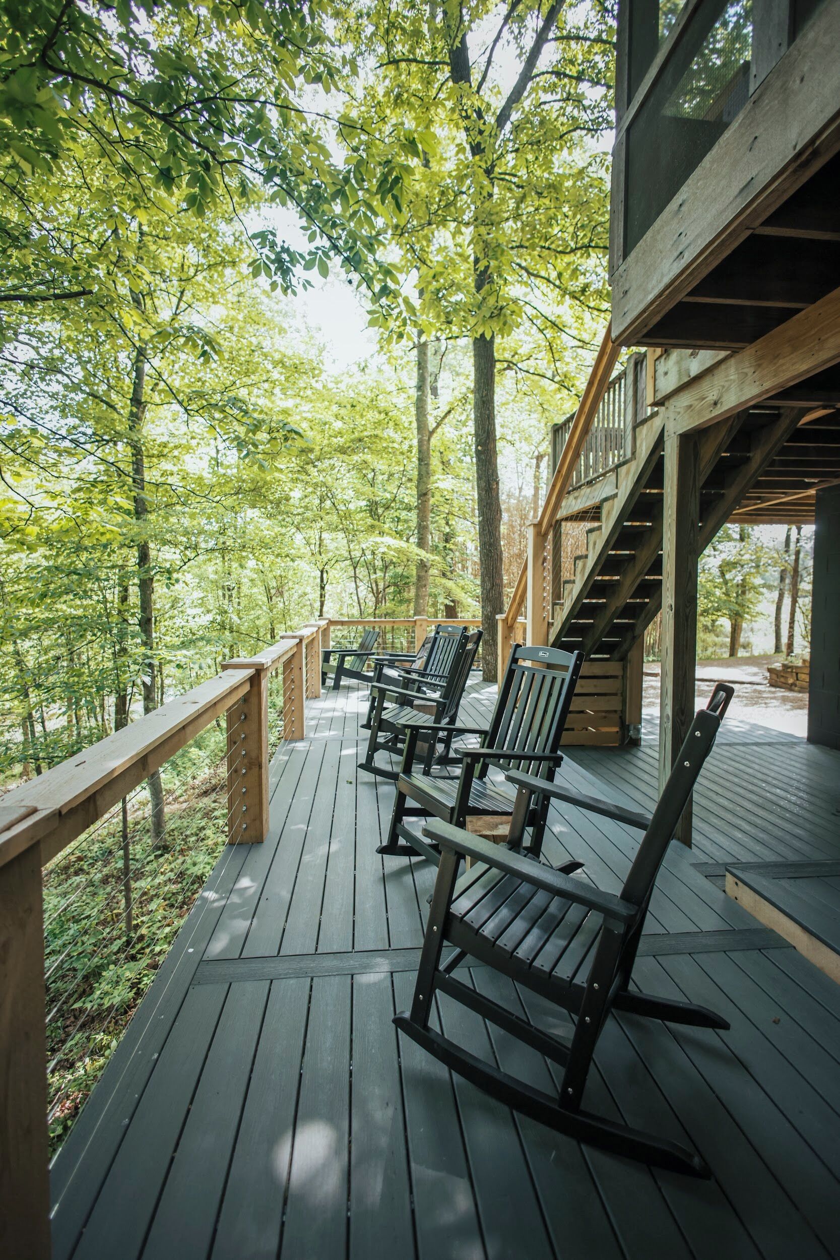 A wooden deck with chairs and a staircase leading to an upper level.