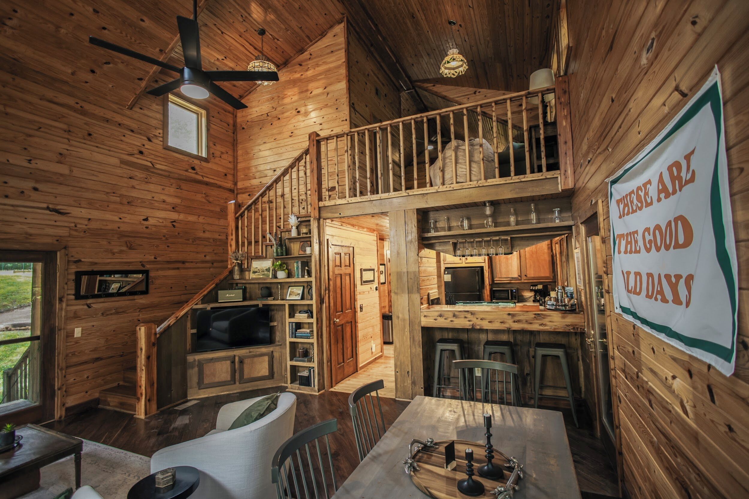 Une cabane en bois spacieuse comprenant un coin repas, une cuisine et un escalier menant à une mezzanine.