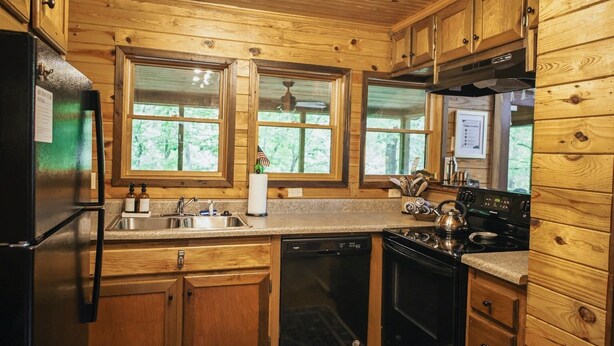 A compact kitchen with wooden cabinets, a refrigerator, a stove, and a dishwasher. - Private Cabin · Creekside · Hot tub · Fire pit · Only 1hr to Nashville (Nunnelly)