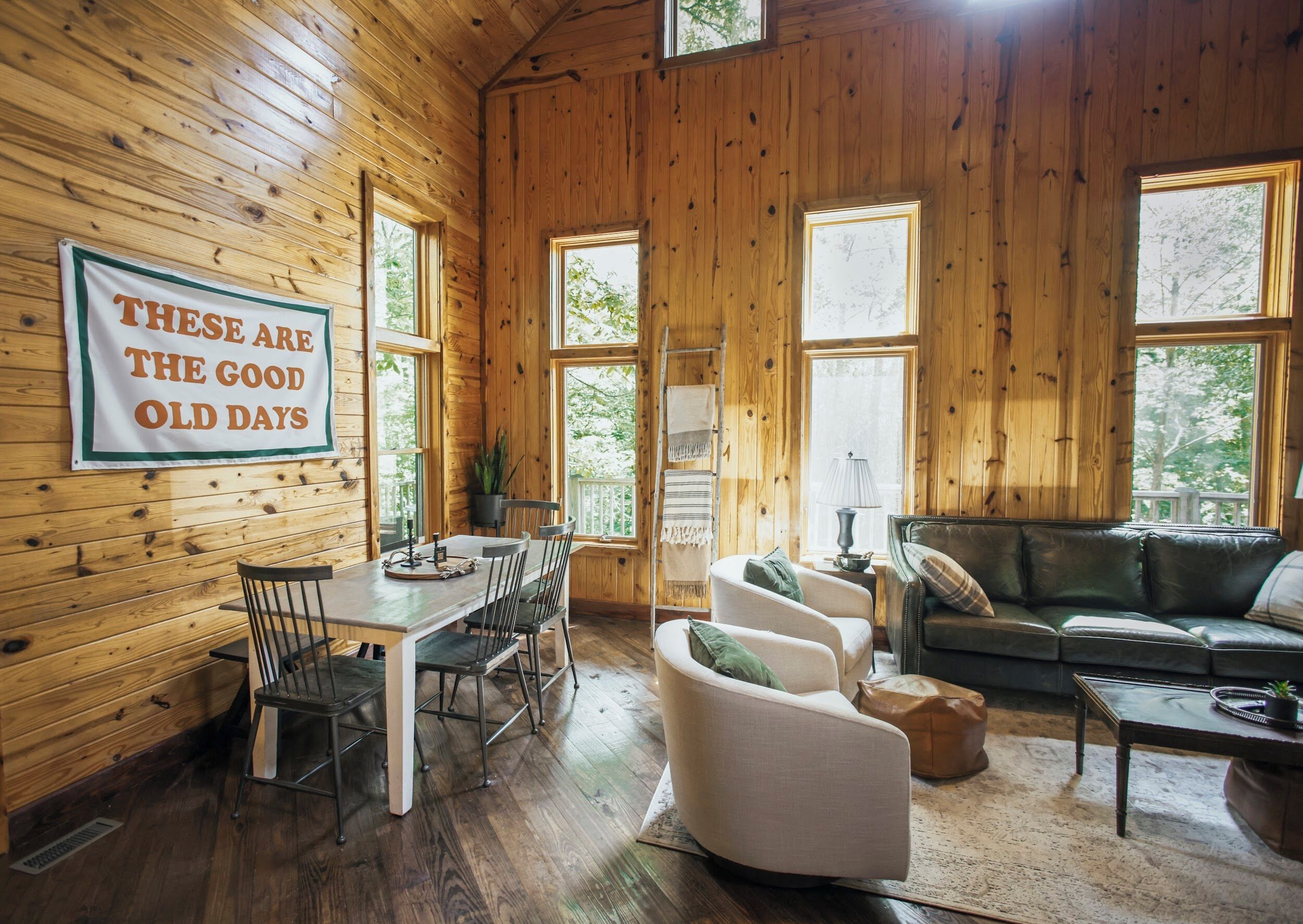 A cozy cabin interior with a dining area, a sofa, and a large window.