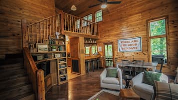 A wooden cabin interior with a staircase, a dining area, and a sign that reads 'These are the good old days.'