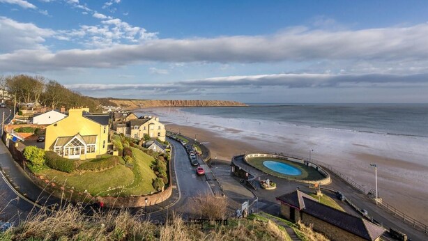 Une ville côtière avec une plage, un rond-point et un bâtiment jaune.