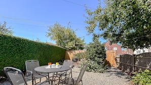 Une terrasse extérieure avec une table ronde et des chaises, entourée d’une zone recouverte de gravier et d’une clôture en bois.
