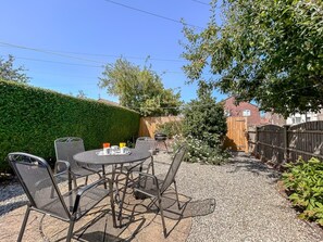 An outdoor patio with a round table and chairs, surrounded by a gravel area and a wooden fence. - 2 Bed in Filey (oc-49508) (Filey)