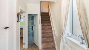 Un escalier dont les marches sont recouvertes de moquette, menant à une pièce dotée d’une fenêtre et d’un radiateur.