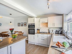 A modern kitchen with white cabinetry, a central island, and a dining area with wooden chairs. - 2 Bed in Filey (oc-49508) (Filey)