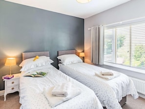 A bedroom with two beds, a nightstand with a lamp, a window with blinds, and a view of greenery outside. - 2 Bed in Filey (oc-49508) (Filey)