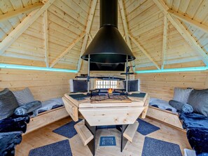 Een gezellig blokhutinterieur met een houtkachel in het midden, houten wanden en een schuine kap.