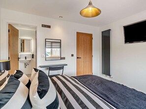 Een slaapkamer met een bed, bureau, stoel, spiegel, deur en televisie.