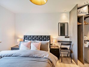 A modern bedroom with a tufted headboard, a bed with grey bedding, bedside lamps, a desk with a chair, and a wardrobe. - 3 Bed in Carlisle (oc-94673) (Arthuret)
