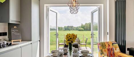 A modern kitchen with a dining area, a view of a green field, and a colorful chair.