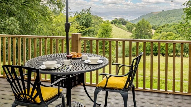 A round table with chairs on a deck, overlooking a scenic landscape.