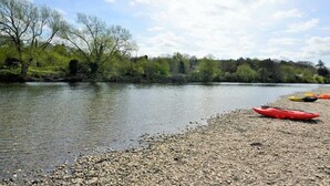A riverbank with kayaks and a pebbly shore.
