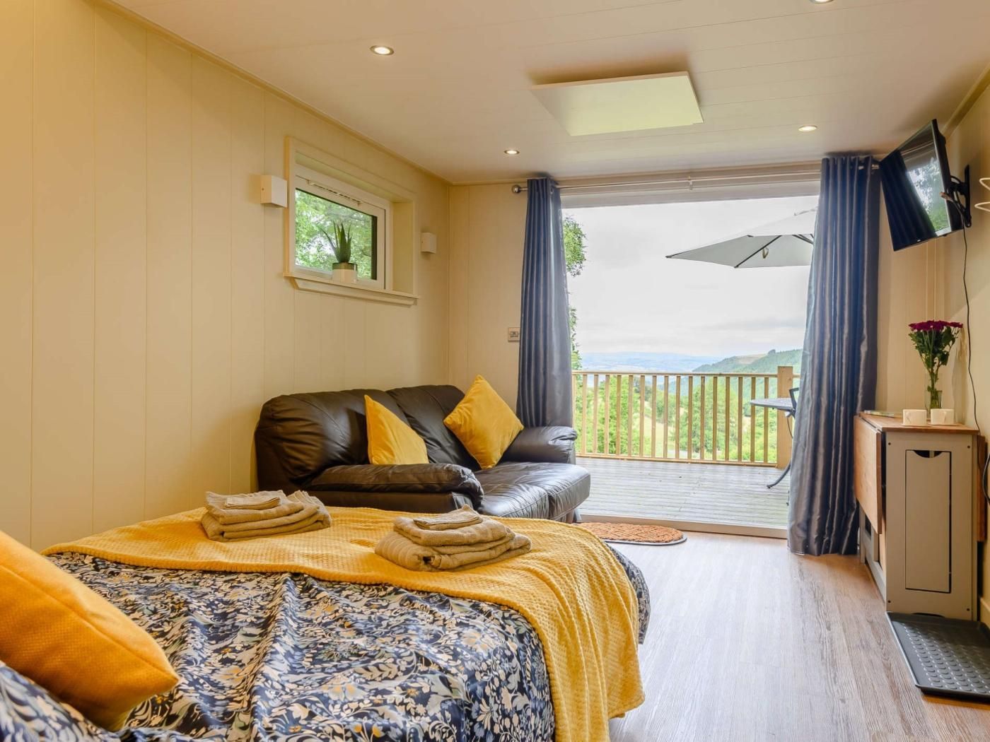 A bedroom with a bed, a sofa, a TV, and a balcony with a view.
