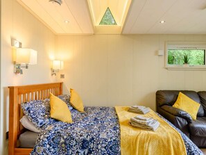 A bedroom with a bed, a sofa, a skylight, and a window with a plant.