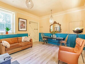 Ein Zimmer mit Holzboden, einem braunen Sofa, einem Esstisch mit Stühlen, einem Spiegel und einer Pendelleuchte.