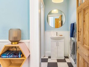 Une salle de bain avec un lavabo blanc, un miroir rond et un carrelage à motifs carrés.
