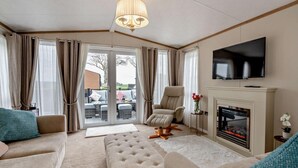 Een woonkamer met een bank, voetenbankje, fauteuil, open haard, televisie en uitzicht door een glazen deur.