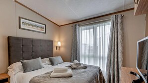 Een hotelkamer met een groot bed, nachtkastje, televisie en raam met gordijnen.