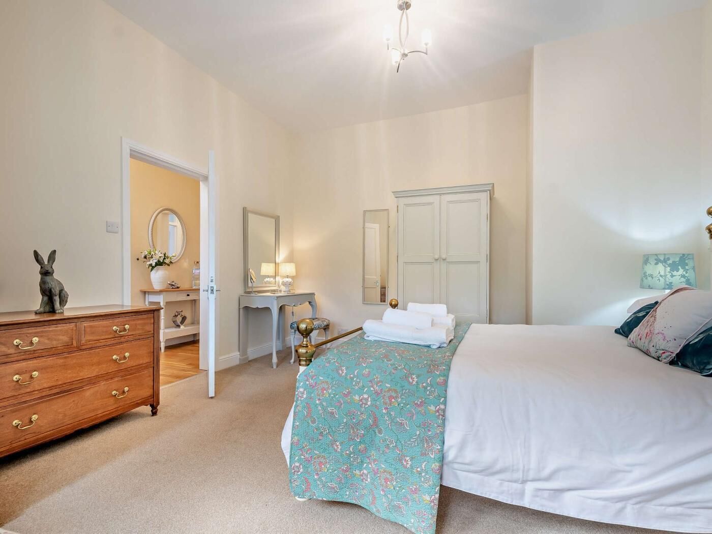 A bedroom with a bed, dresser, vanity, and a wardrobe.