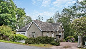 Een stenen huis met twee verdiepingen, een puntgevel, een veranda en een oprit die naar de ingang leidt.