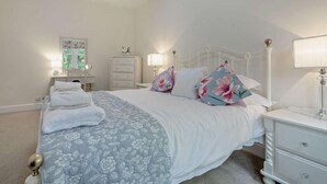 Een slaapkamer met een bed, nachtkastjes, een dressoir, een lamp en een raam met uitzicht.