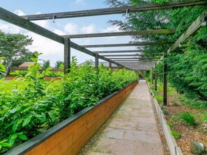 A covered walkway with a stone floor, bordered by a wooden fence and lush green plants. - 2 Bed in Malton (oc-87936) (West Heslerton)