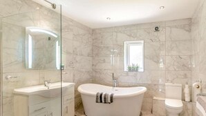Et moderne badeværelse med et fritstående badekar, en glasafskærmet brusekabine, et kommode med skuffer og et toilet.