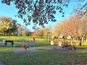 Ein Park mit Spielgeräten, einer Bank und Bäumen.