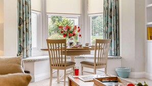 A cozy room with a bay window, two wooden chairs, a table with a vase of flowers, and a window seat. - 2 Bed in Filey (oc-85246) (Filey)