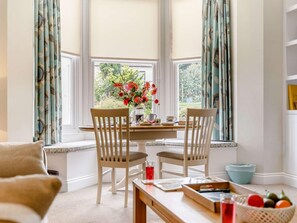 Ein gemütliches Zimmer mit Erker, zwei Holzstühlen, einem Tisch mit Blumenvase und einer Sitzbank am Fenster.