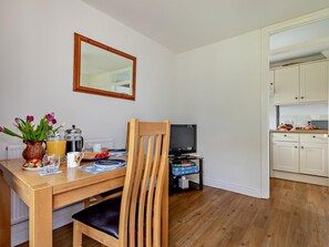 A dining area with a wooden table, chairs, and a television in the background. - 1 Bed in Wells (oc-94958) (Wookey)