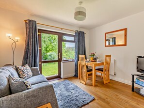A modern living room with a sofa, dining table, chairs, a TV, and a large window with curtains. - 1 Bed in Wells (oc-94958) (Wookey)